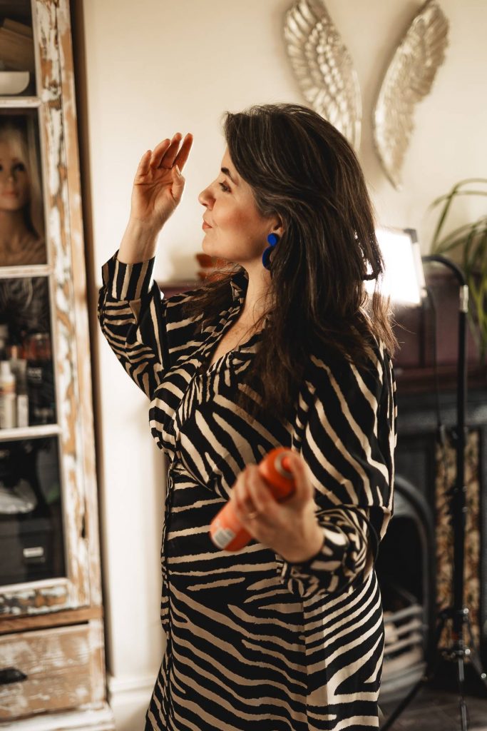 Behind-the-scenes image of a midlife woman adjusting hair and preparing for personal brand photoshoot. Authentic behind-the-scenes moment during a personal brand photoshoot, reflecting the journey of overcoming fear and embracing confidence at 47.